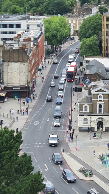 Aerial view of a residential street with a row of terraced houses featuring brick and light-colored facades, some with bay windows and pitched roofs fitted with skylight windows. Cars are parked along